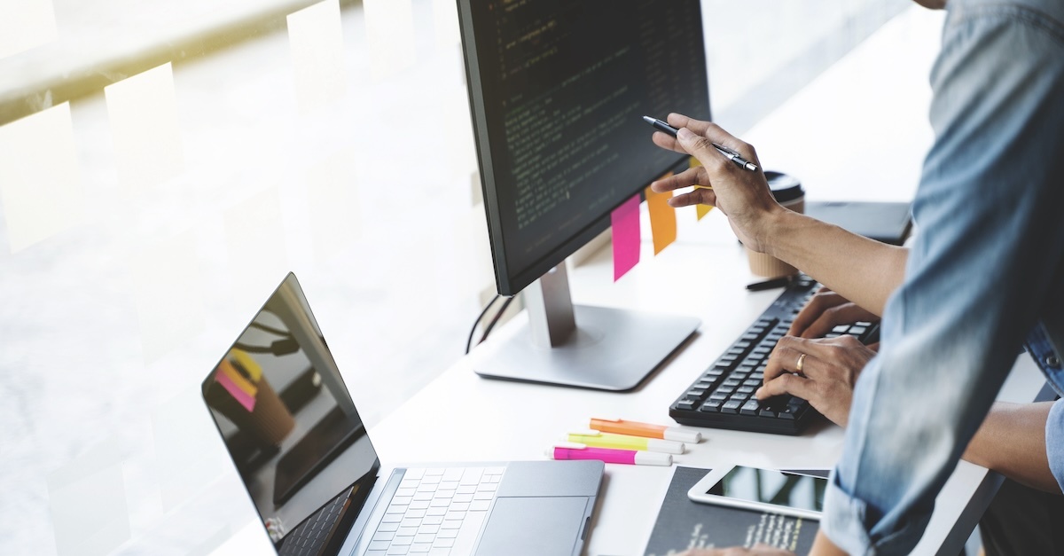 A man in an IT career works at a desk with laptop and monitor