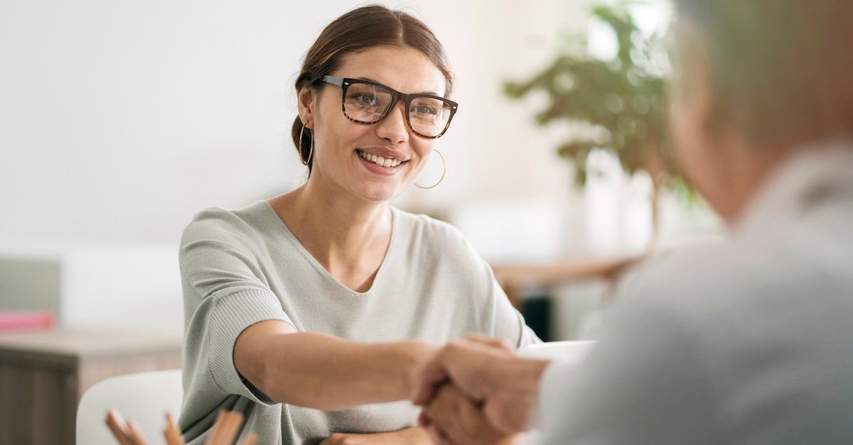 A woman in glasses and a grey blouse giving handshake