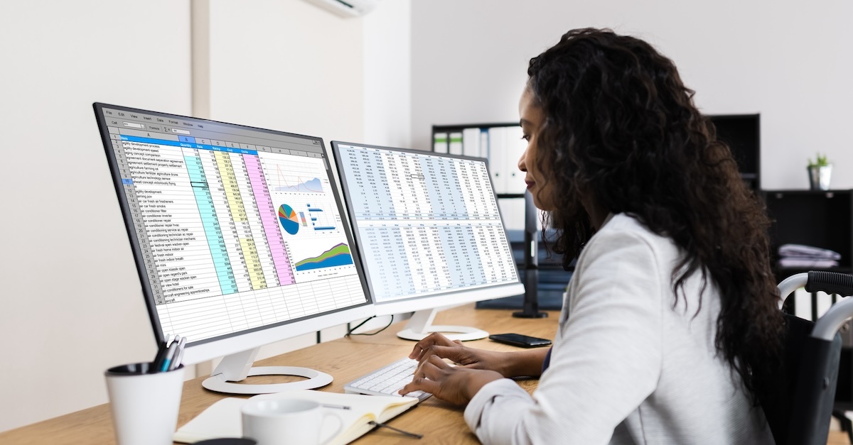 woman working on spreadsheets at a desk with two monitors