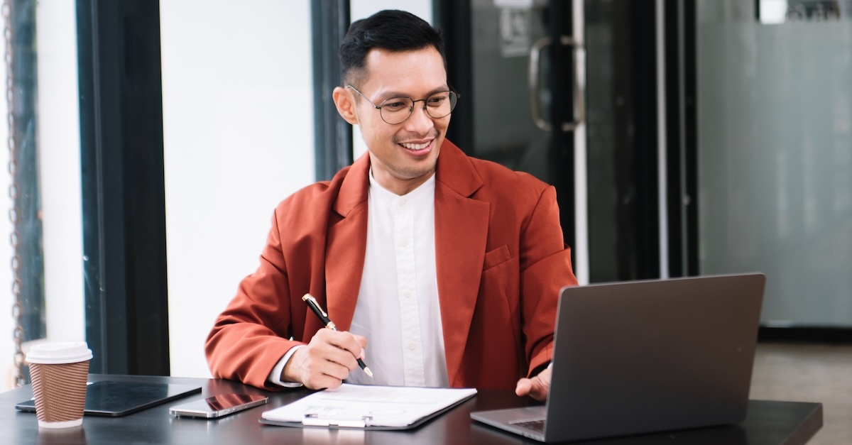 Man working at desk with pen, paper, and a laptop