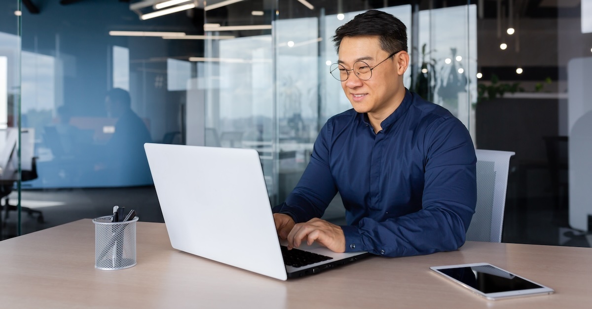 man working at a workplace at a desk with a laptop and tablet.