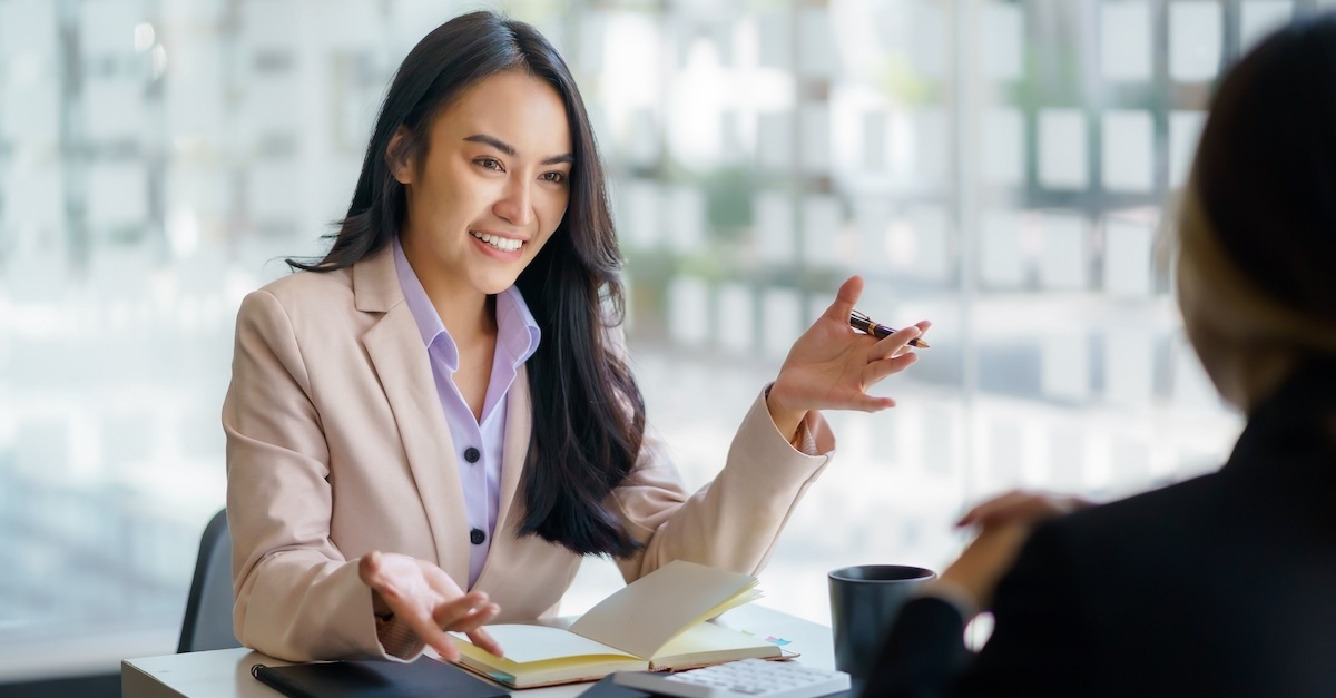 Woman giving an elevator pitch at a work table with a notepad.