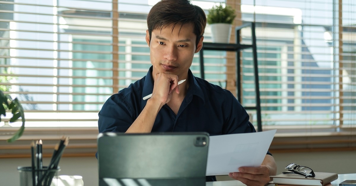 man doing admin tasks at a desk with the blinds open behind him