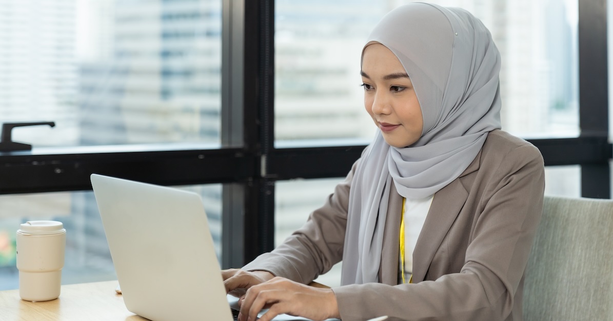 a woman wearing a hijab types on a laptop