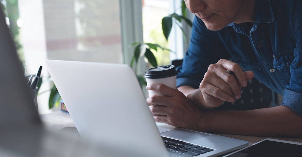 man with coffee looking at laptop