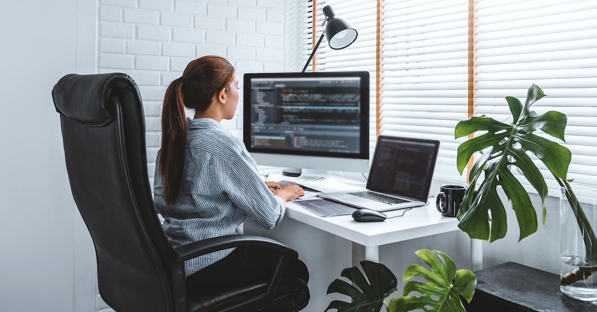 woman working from home coding on a laptop and second monitor