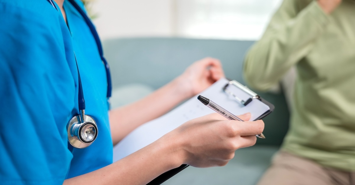 nurse in blue scrubs with a clipboard talking to a patient