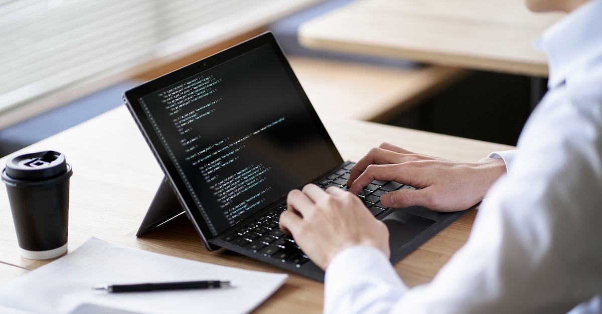 Man in a white shirt coding on a laptop