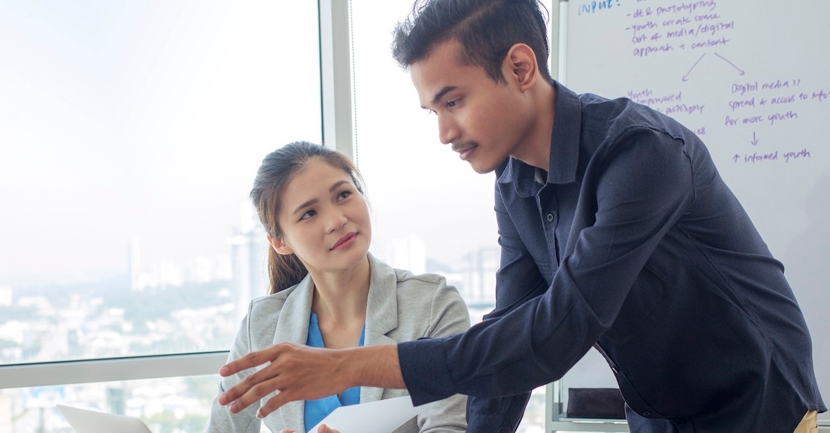 man in a blue shirt talking to a woman at her desk