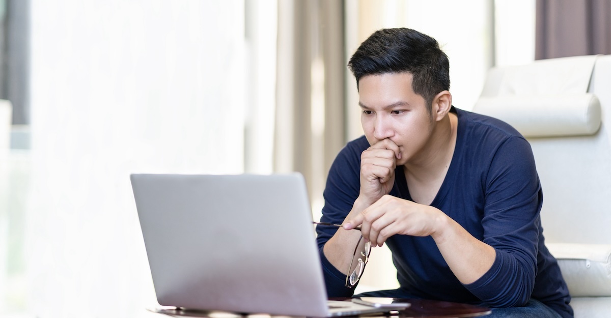 a man looks at a laptop in deep thought while holding a pair of eyeglasses
