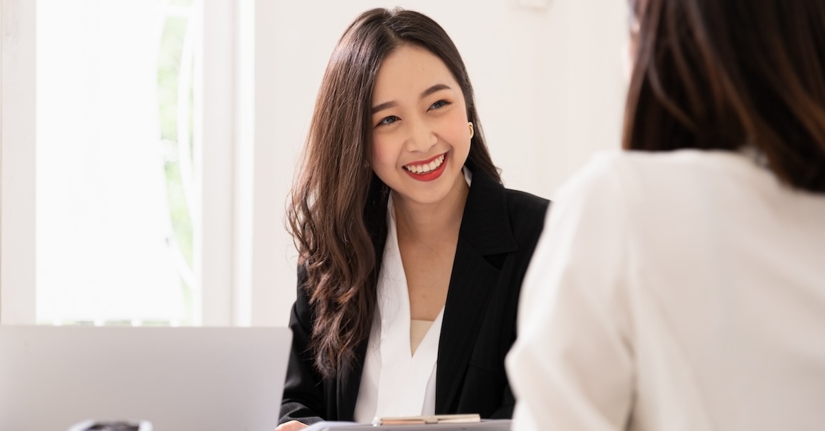 A smiling woman in a professional setting engages in a conversation with another person across the table.