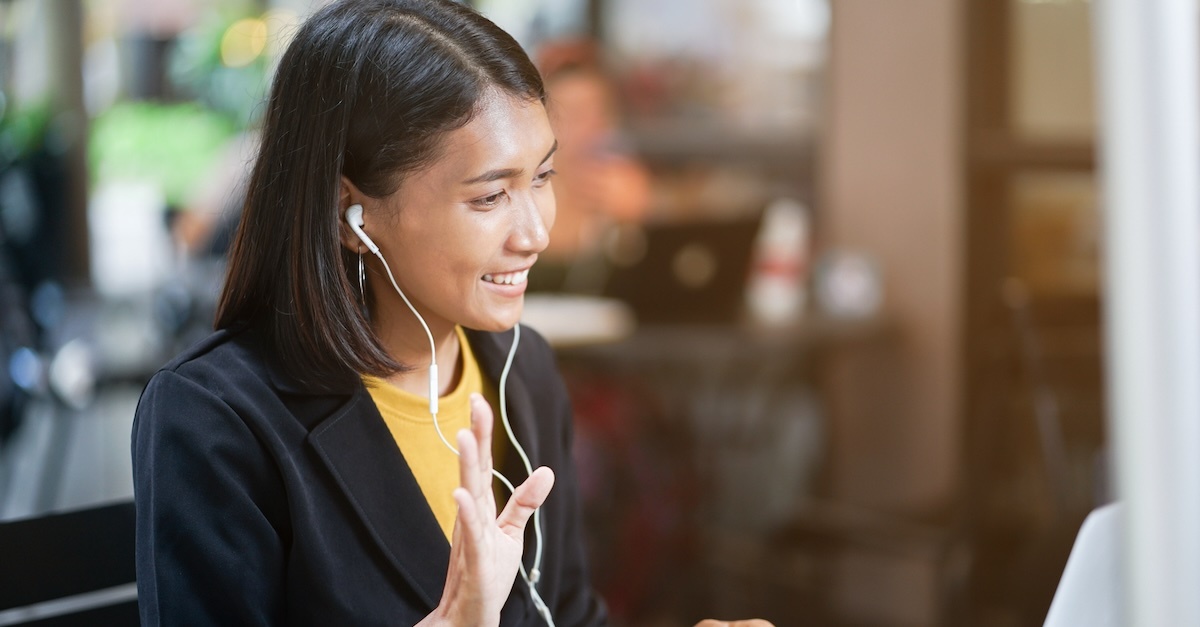 Asian woman with headphones waving during a virtual interview