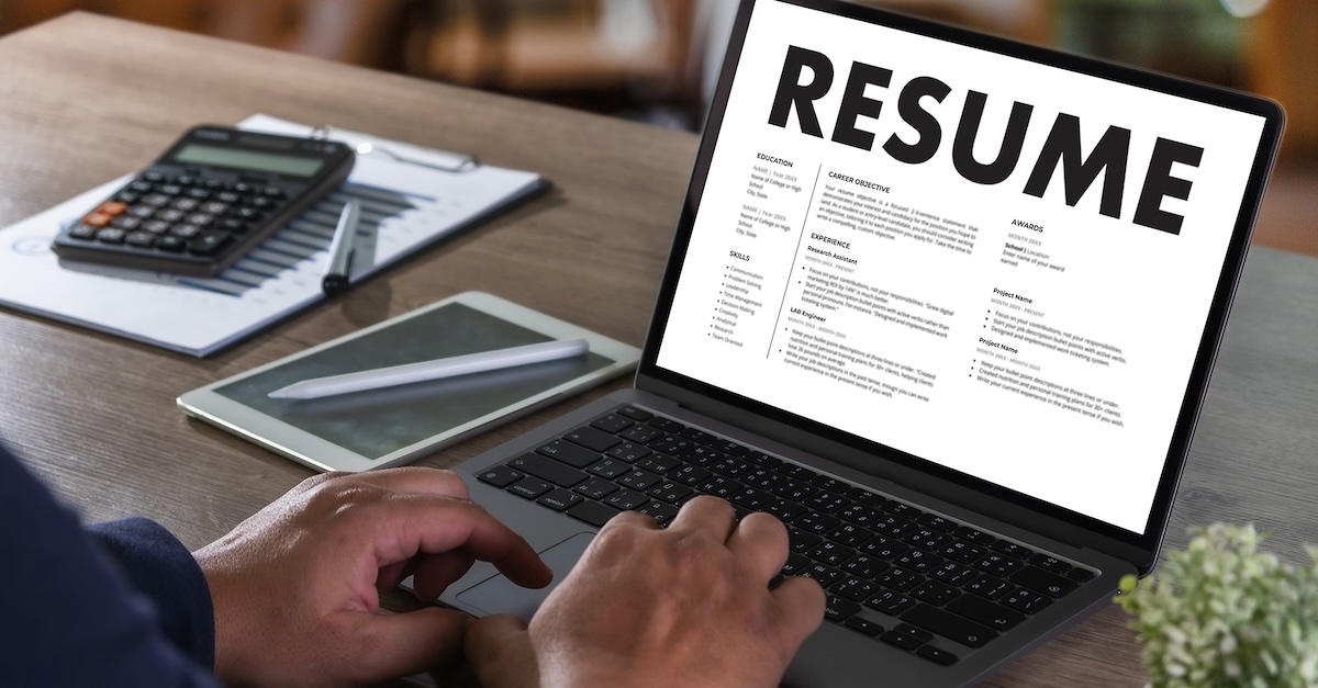 resume on a laptop screen with man typing with a tablet, calculator, and notepad on his desk