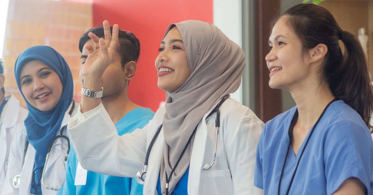 Four nurses during nursing school with one raising her hand with a question.