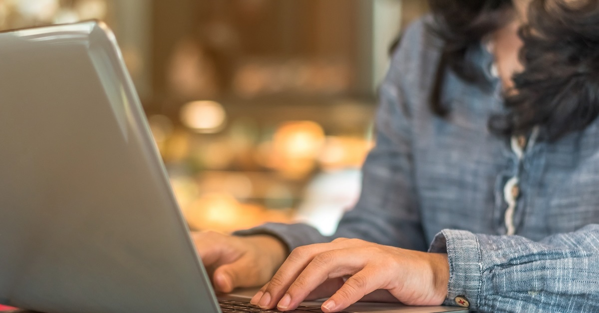 A woman in a blue blouse typing a job offer on a laptop