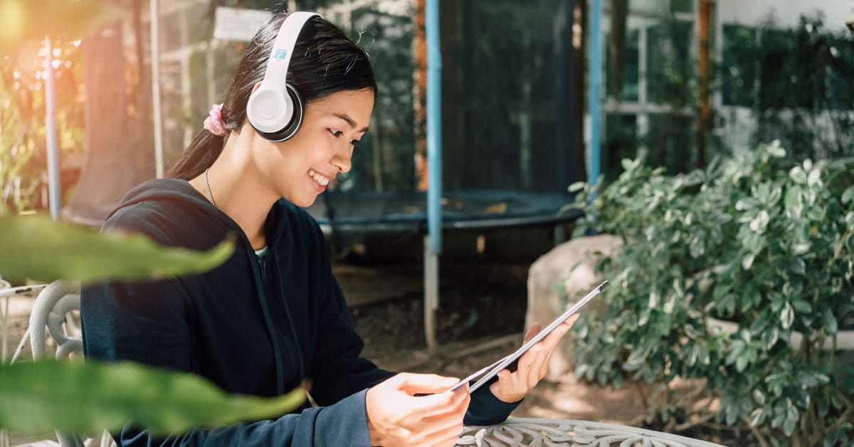 A female freelancer working outside while on a headphones and tablet
