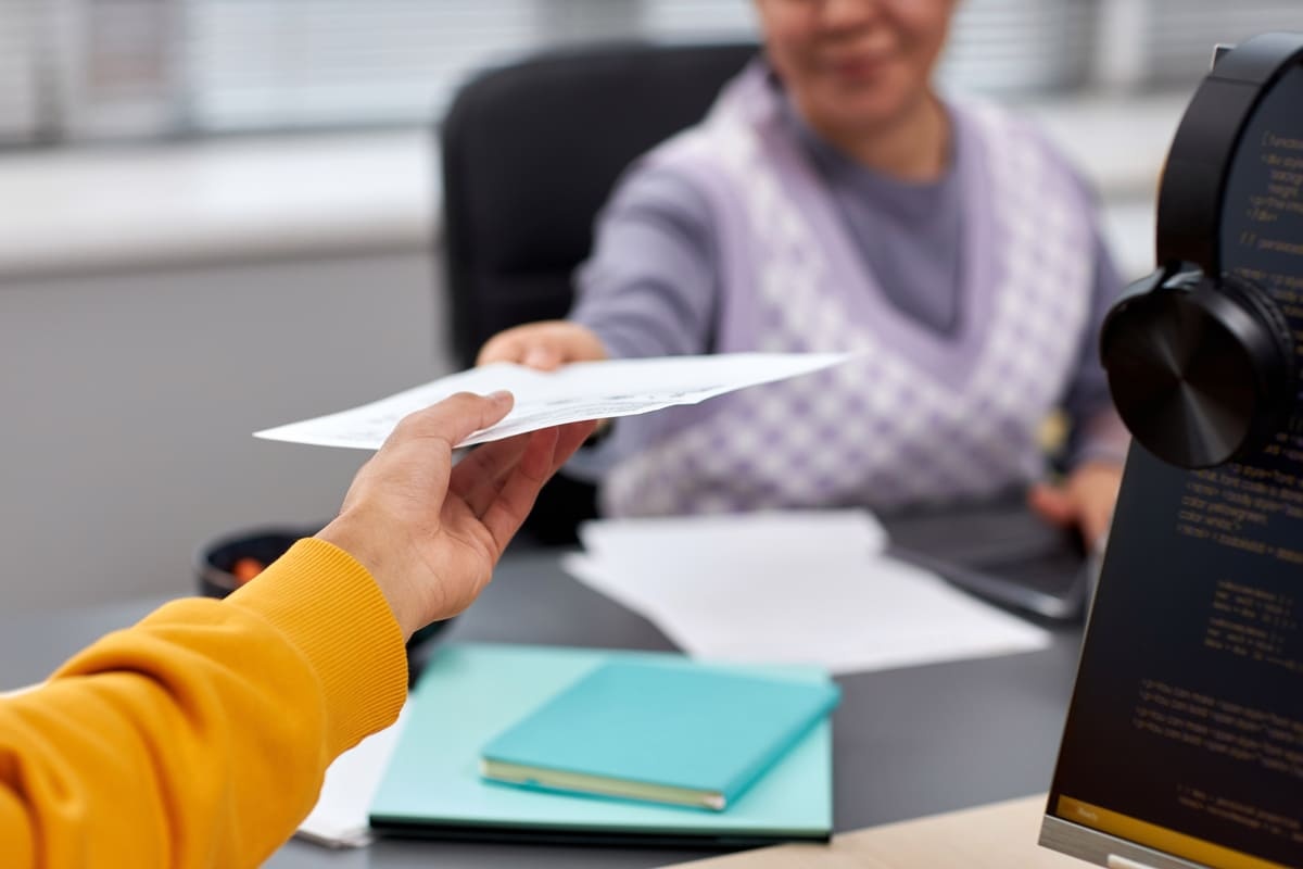 Seorang karyawan wanita menyerahkan surat undangan rapat ke rekan kerjanya.