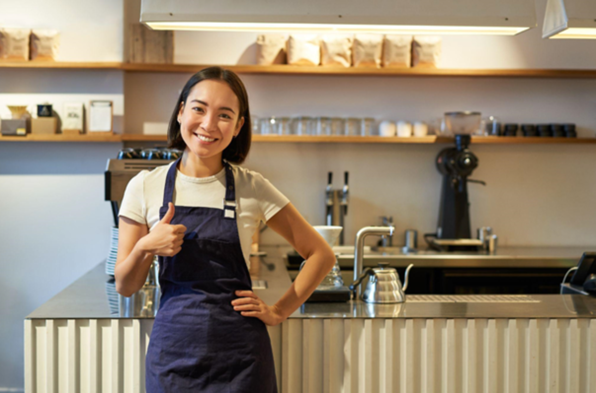 Smiling girl in apron working as cafe barista shows thumbs-up