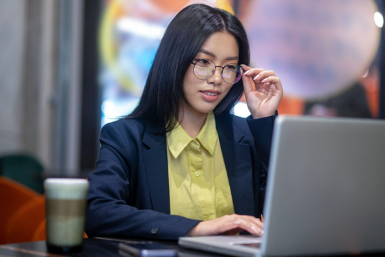 Asian woman in front of laptop adjusting her glasses