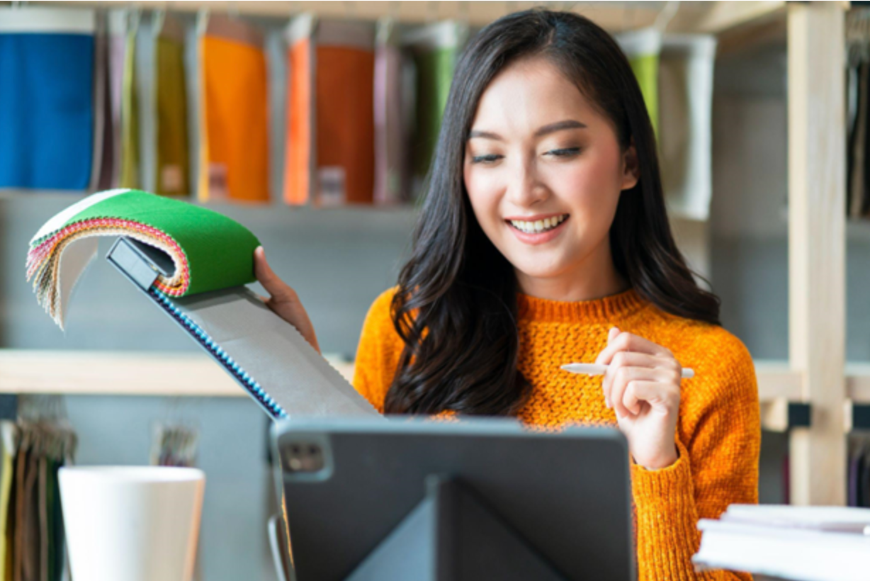 Smiling Asian woman flips open notepad while looking at tablet screen