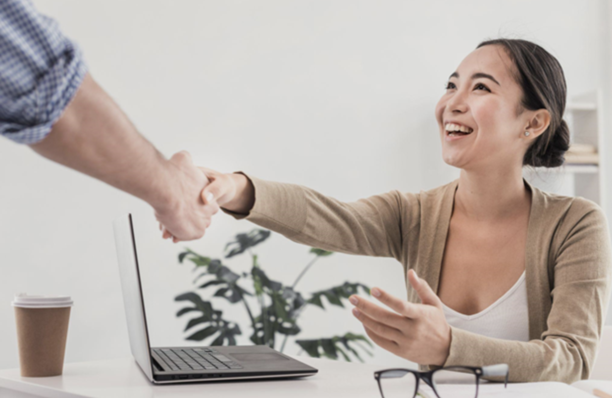 Smiling Asian woman seated at a table shaking hands