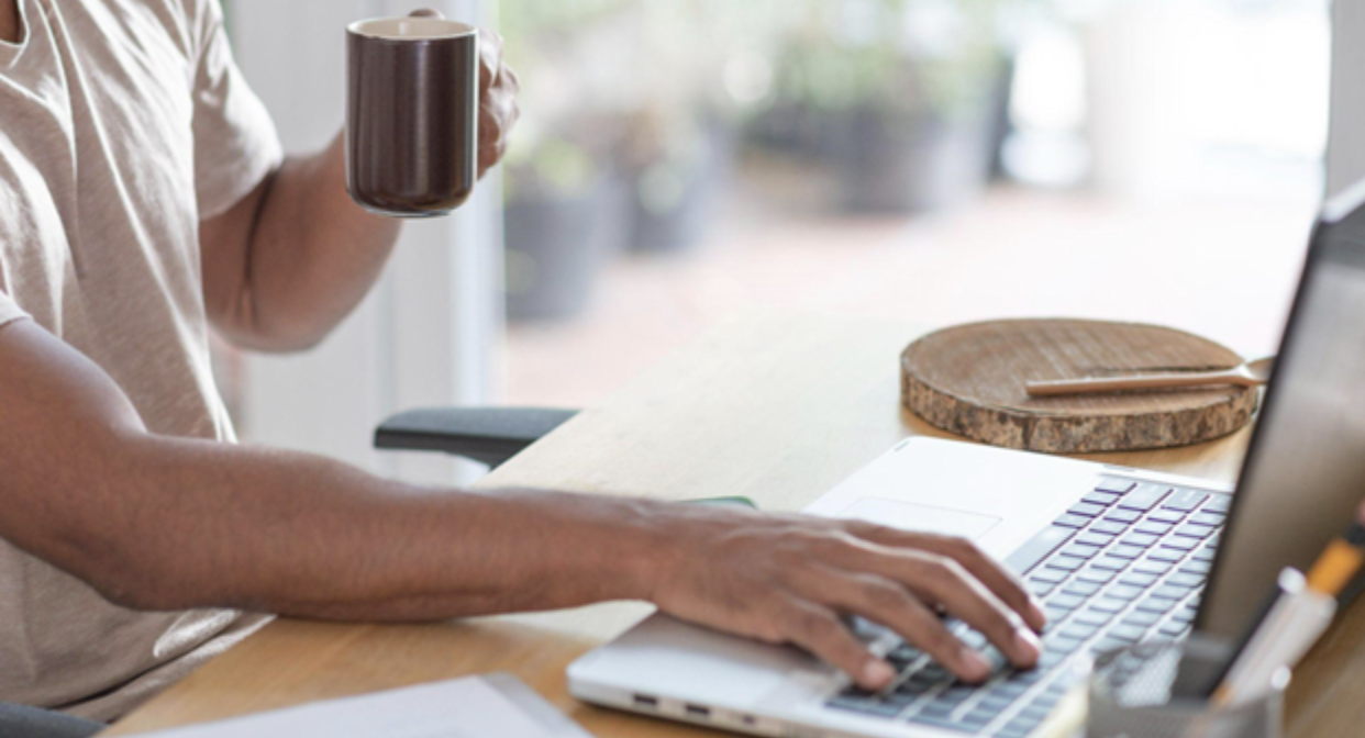 Man typing on laptop with right hand while holding a cup in left hand