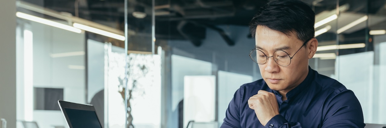 A man wearing a dark blue shirt and glasses working in an office