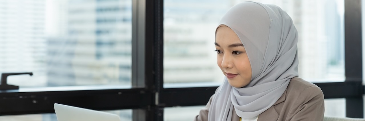 Asian woman looking at laptop wearing a grey hijab