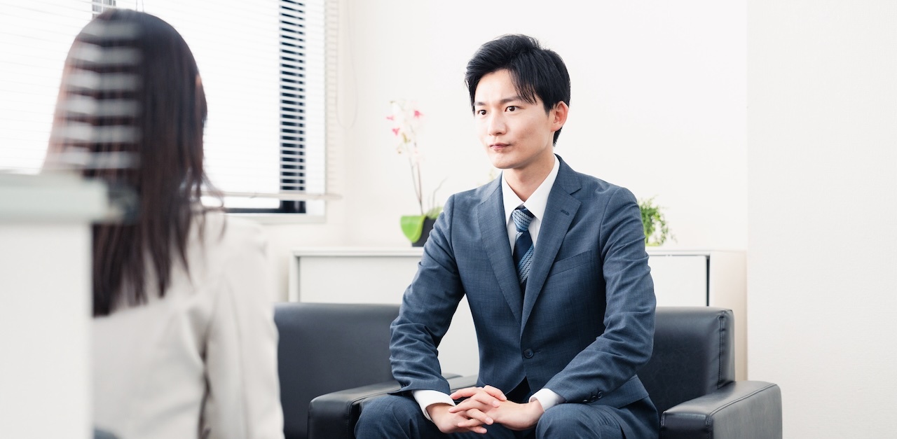 Man in a suit sitting down for an interview with a woman