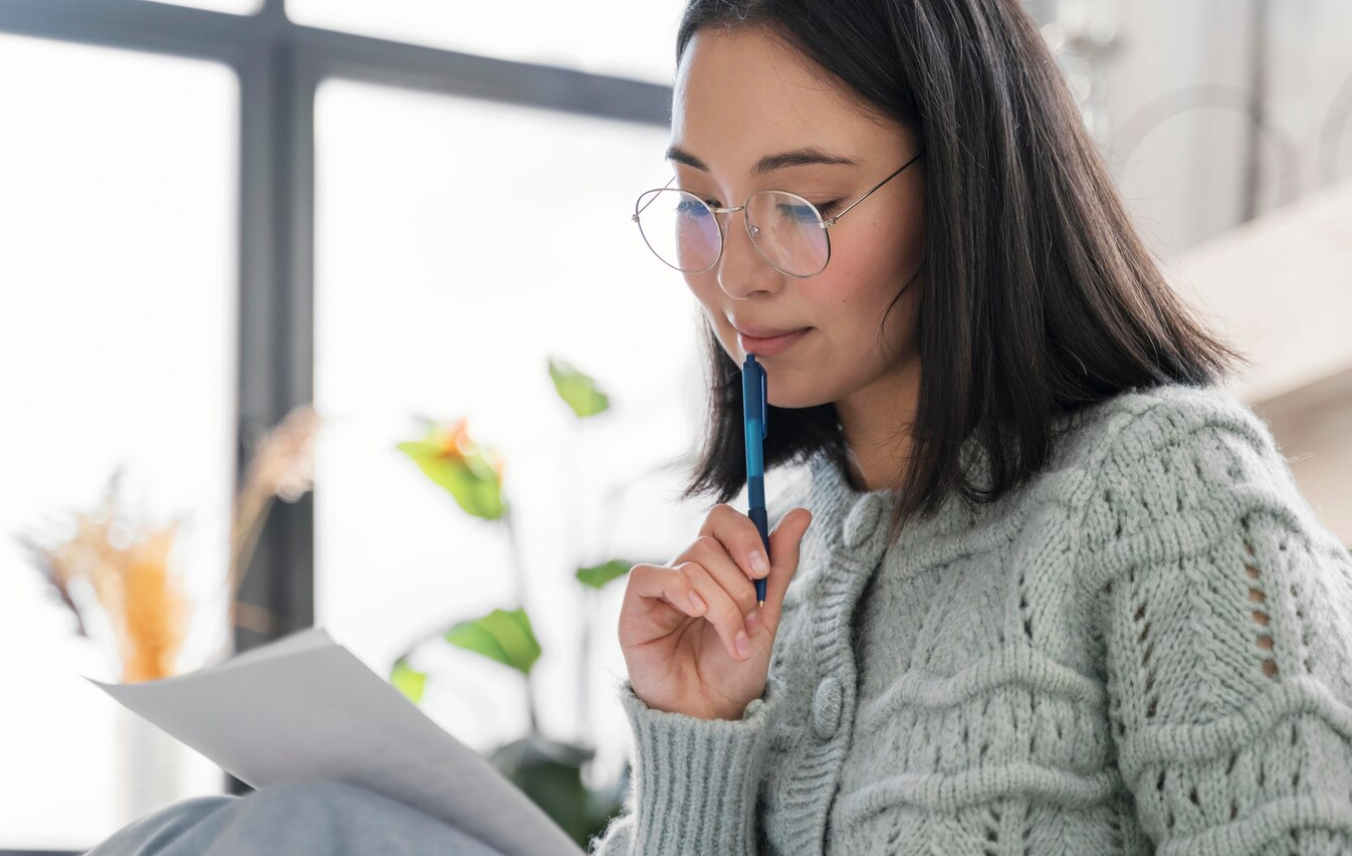 Woman in thought, holding pen to her chin while looking at paper