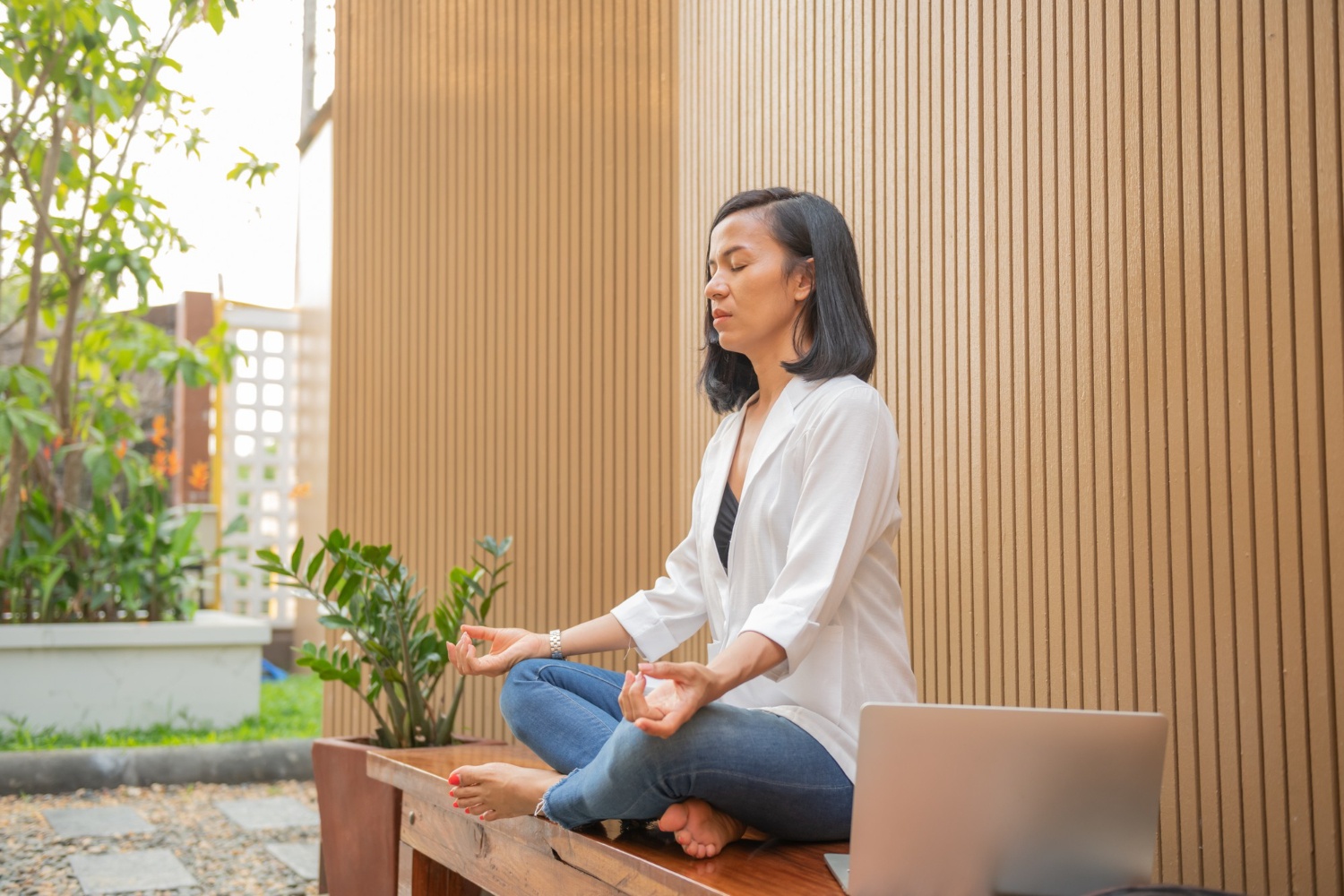 Asian woman sitting cross-legged on bench and meditating