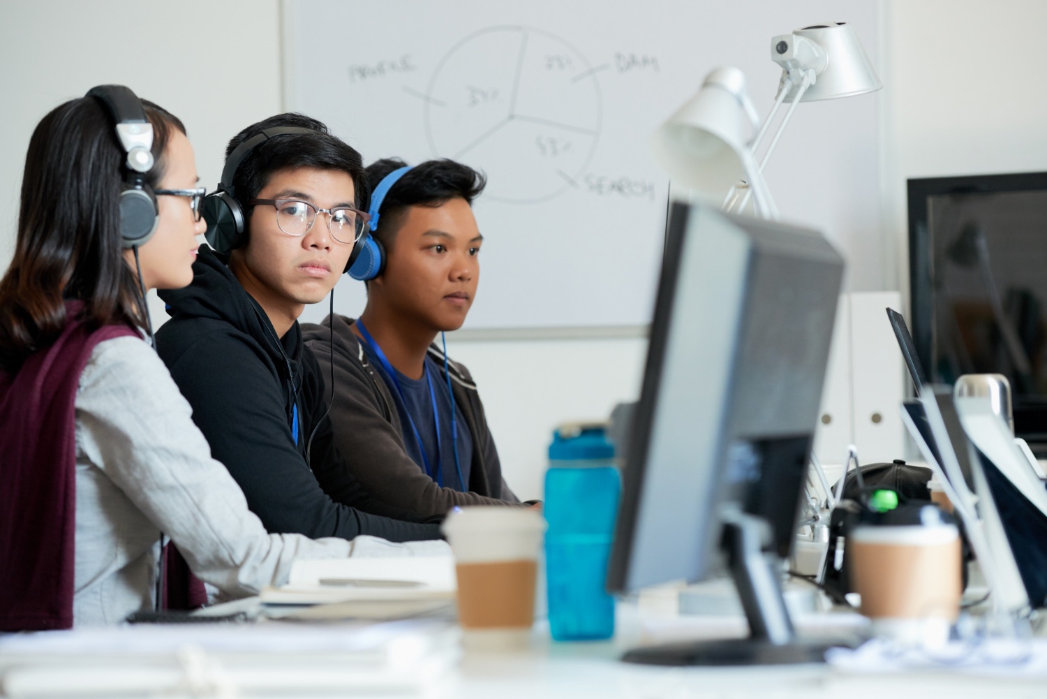 Tiga data analyst mengenakan headphone duduk di depan komputer. (Image by pressfoto on Freepik)