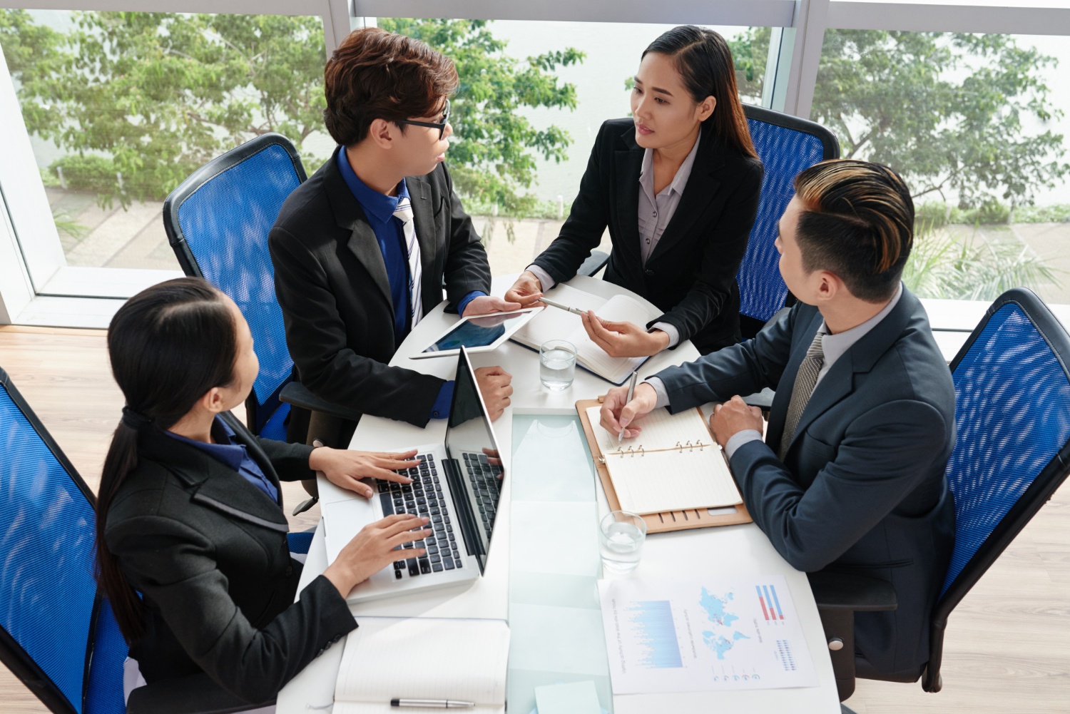 Empat orang berjas sedang duduk di ruangan kantor lengkap dengan laptop dan buku catatan berdiskusi tentang B2B