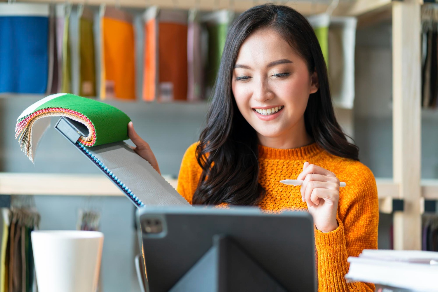 Smiling Asian woman flips open notepad while looking at tablet screen