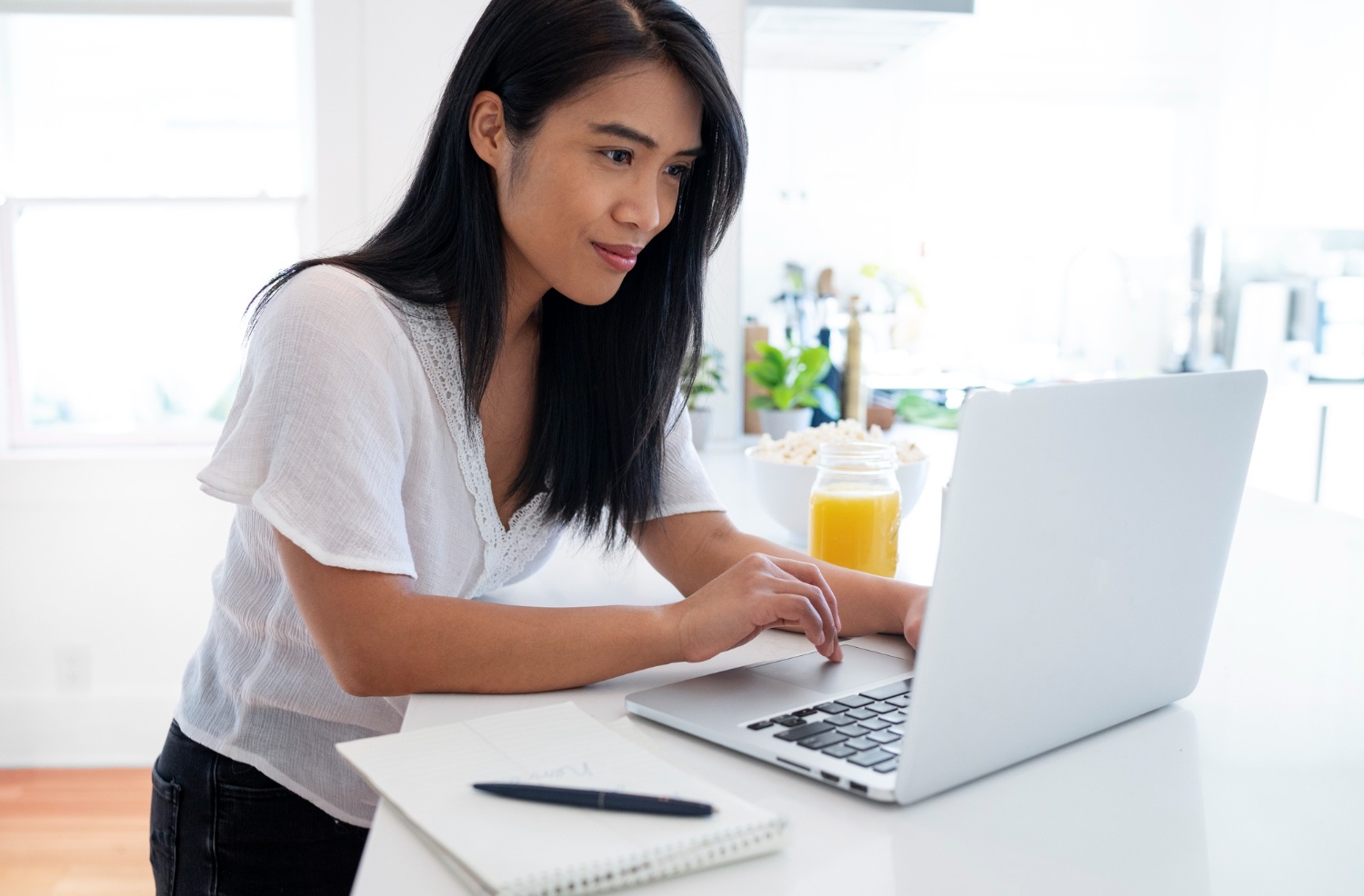 Young Asian woman typing on laptop with a notebook and pen beside her