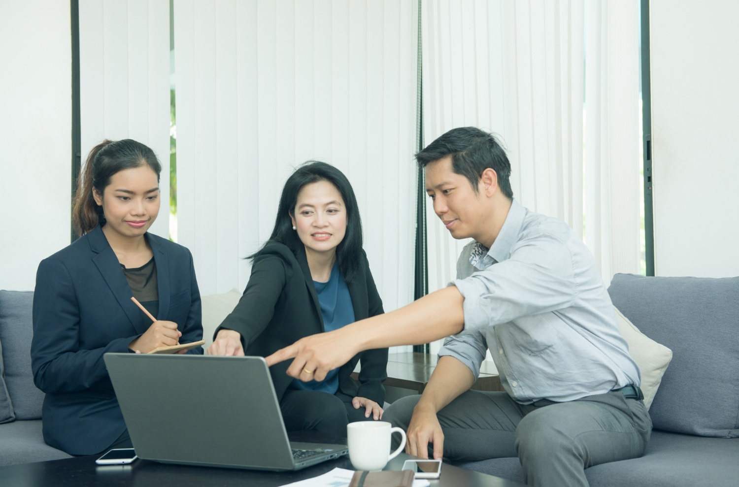 Tiga orang di ruang kantor; dua orang wanita dan satu lelaki; satu wanita siap mencatat, dua orang lainnya menjunjuk laptop membicarakan SOP kerja