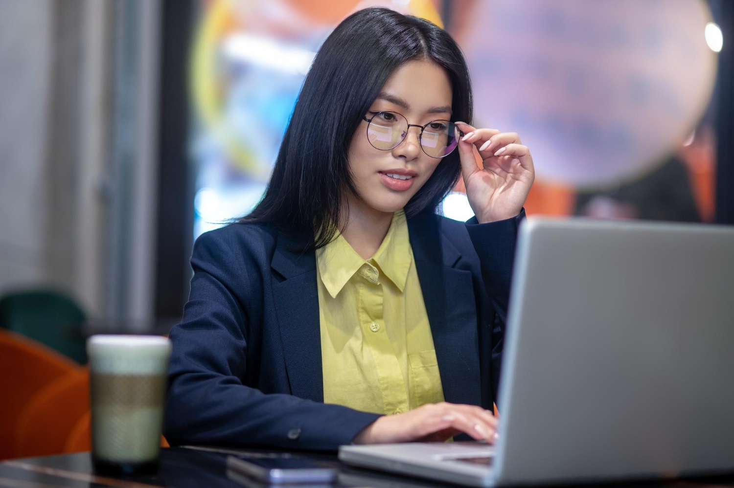 Asian woman in front of laptop adjusting her glasses