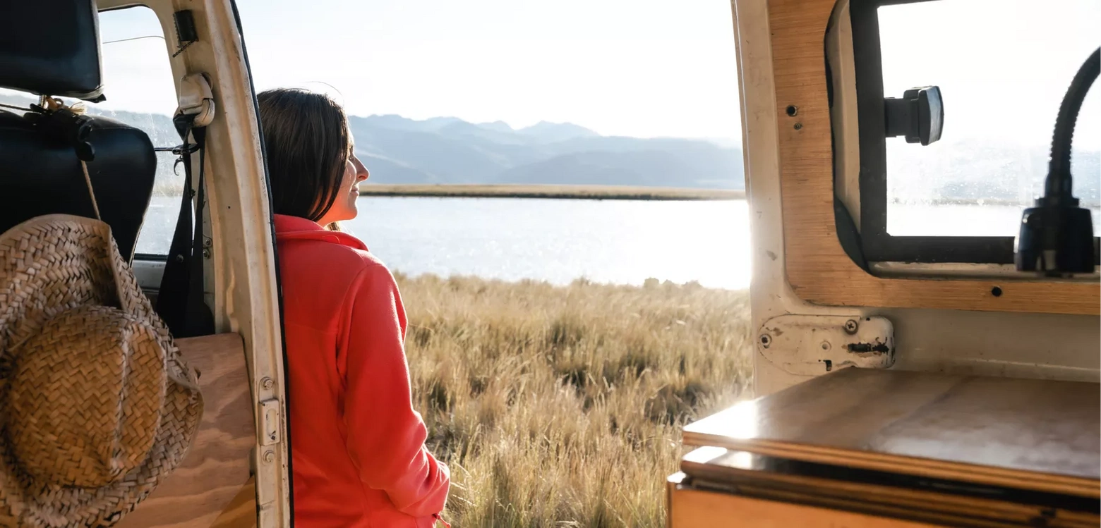 photo of a woman looking out onto a body of water from outside a camping van