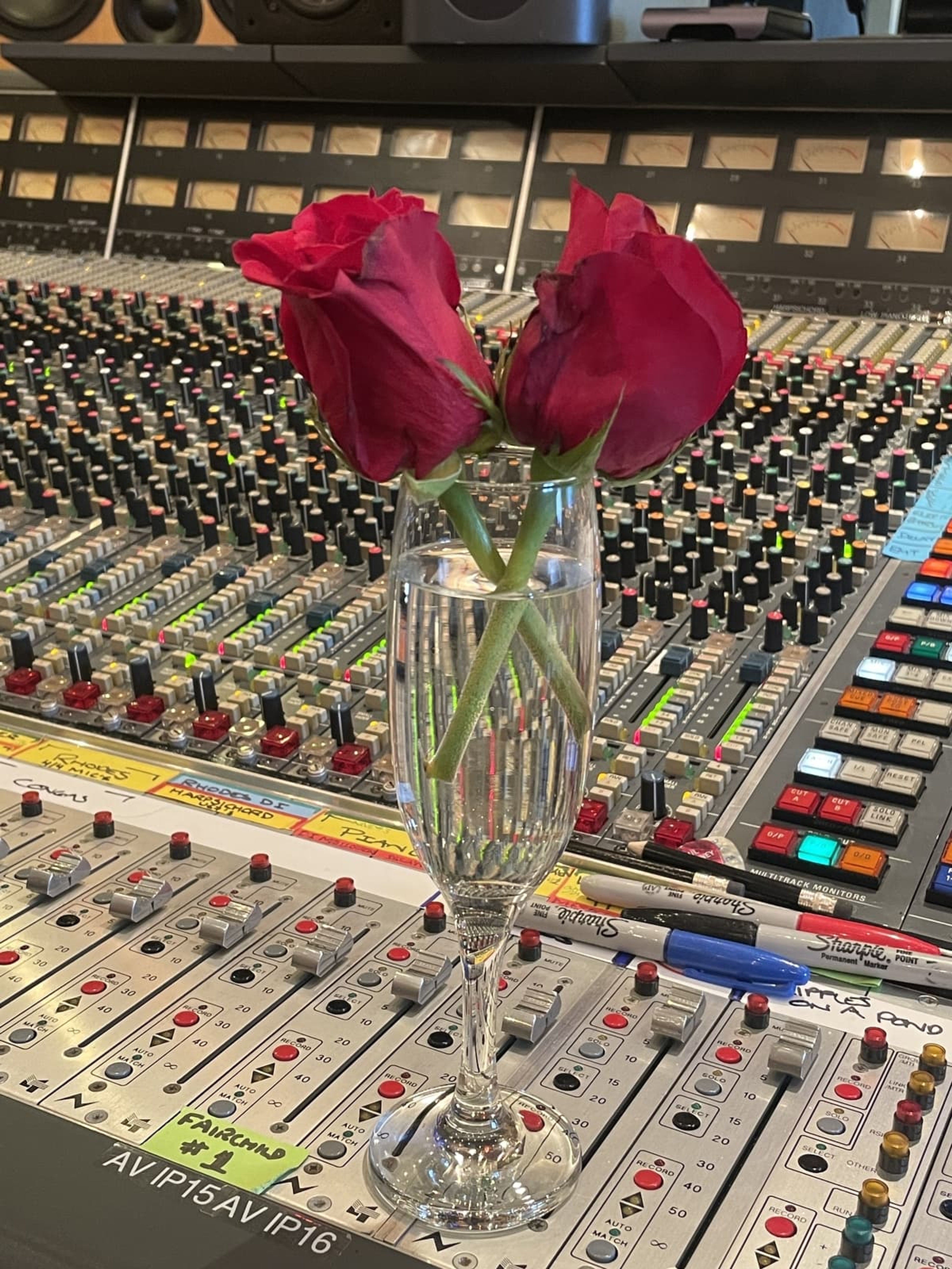 Two roses in a champagne glass, perched on a mixing desk