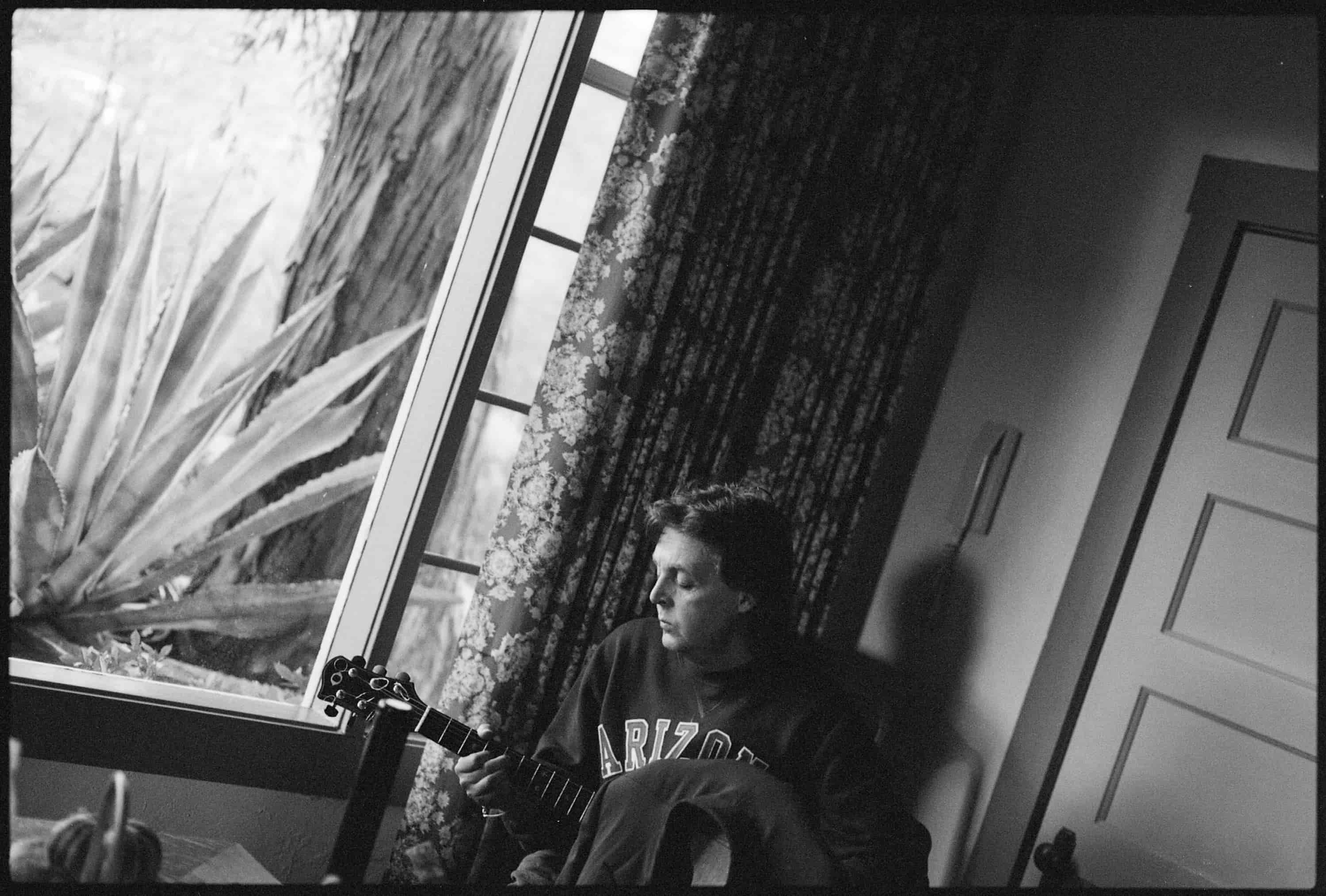 Black and white photo of Paul looking out a window in Arizona with his guitar