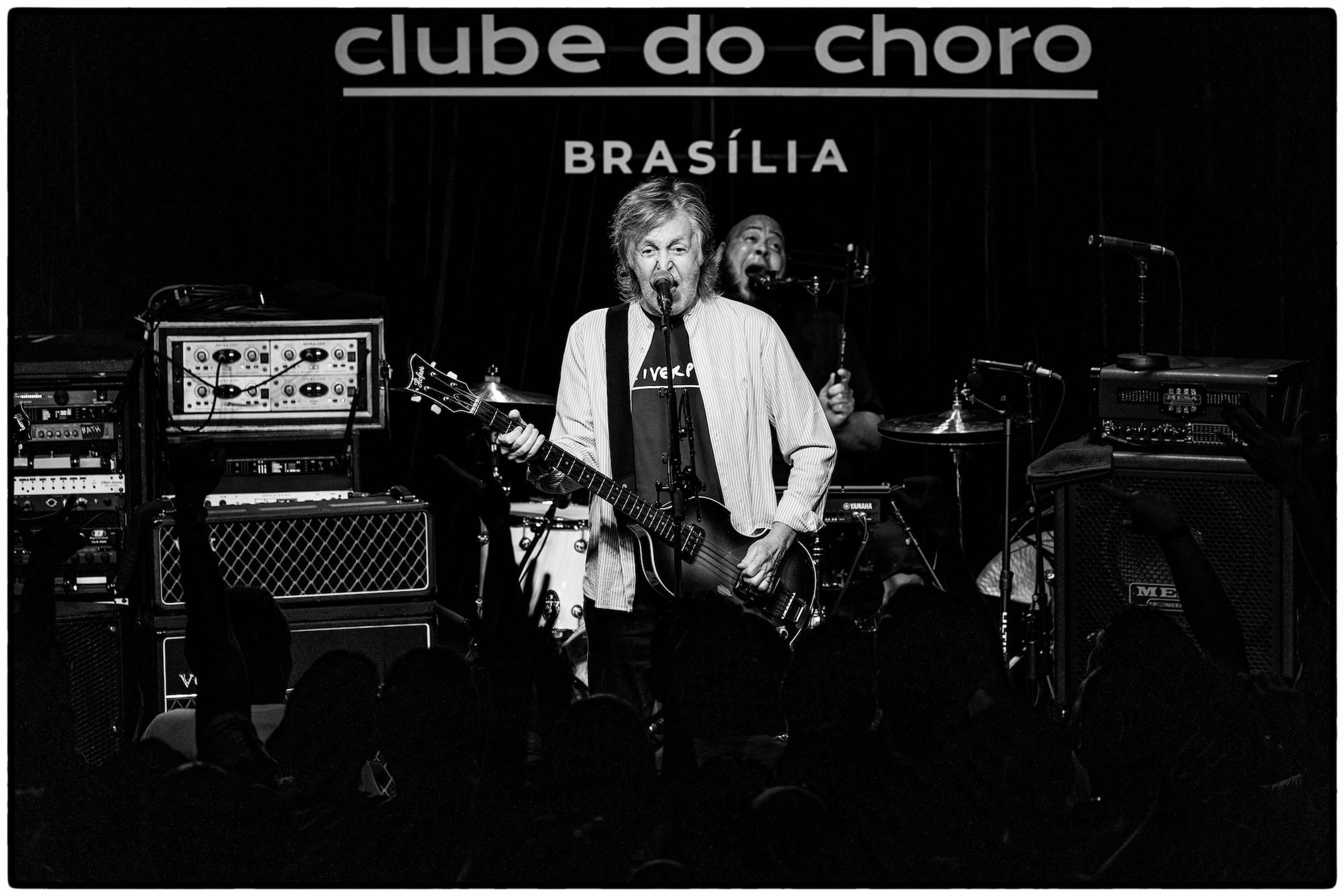 Black and white photo of Paul singing into a microphone on stage at Brasília’s Clube do Choro 