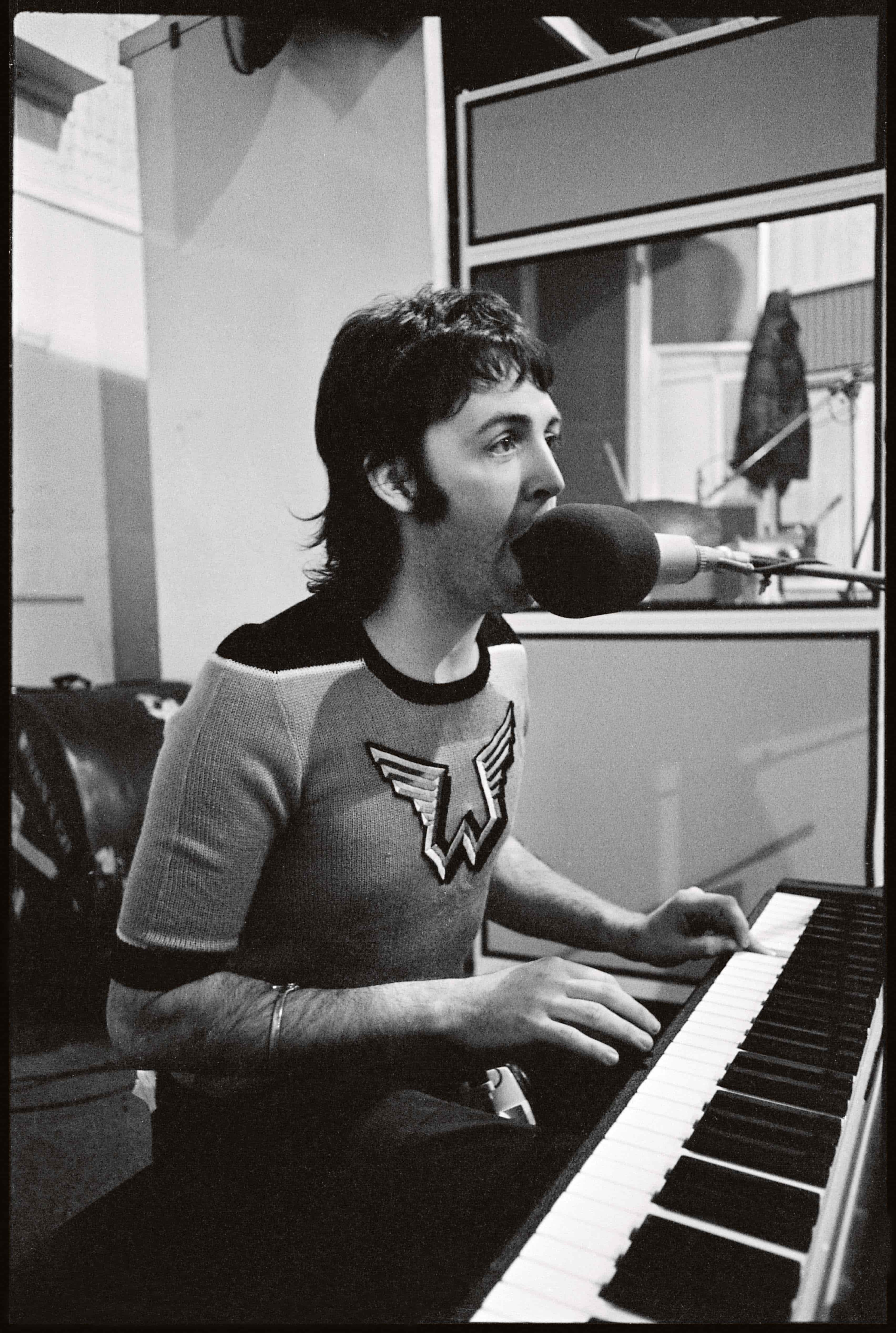 Black and white photo of Paul wearing a Wings t-shirt singing at a piano