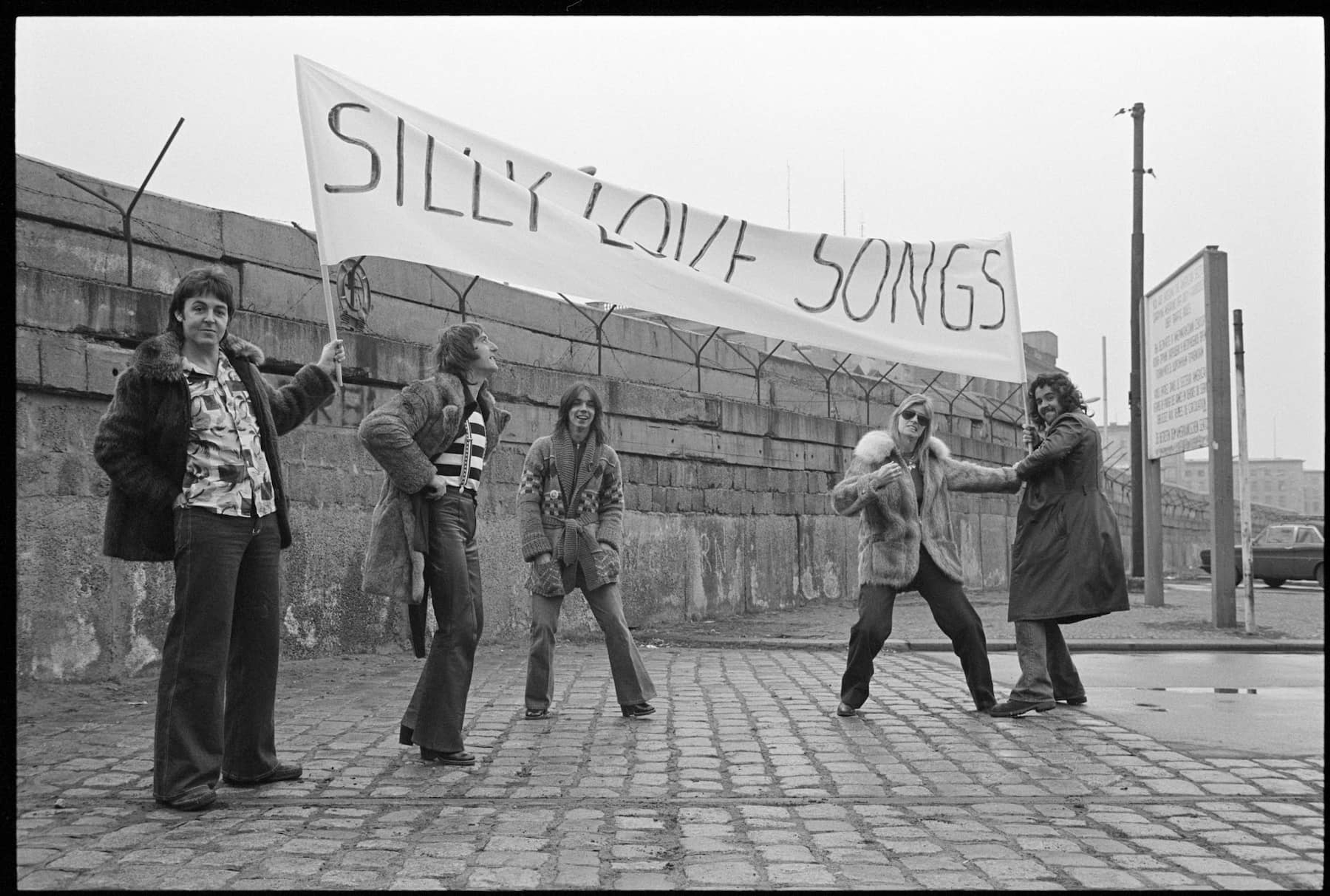 Members of Wings hold up a banner which reads 'SILLY LOVE SONGS'