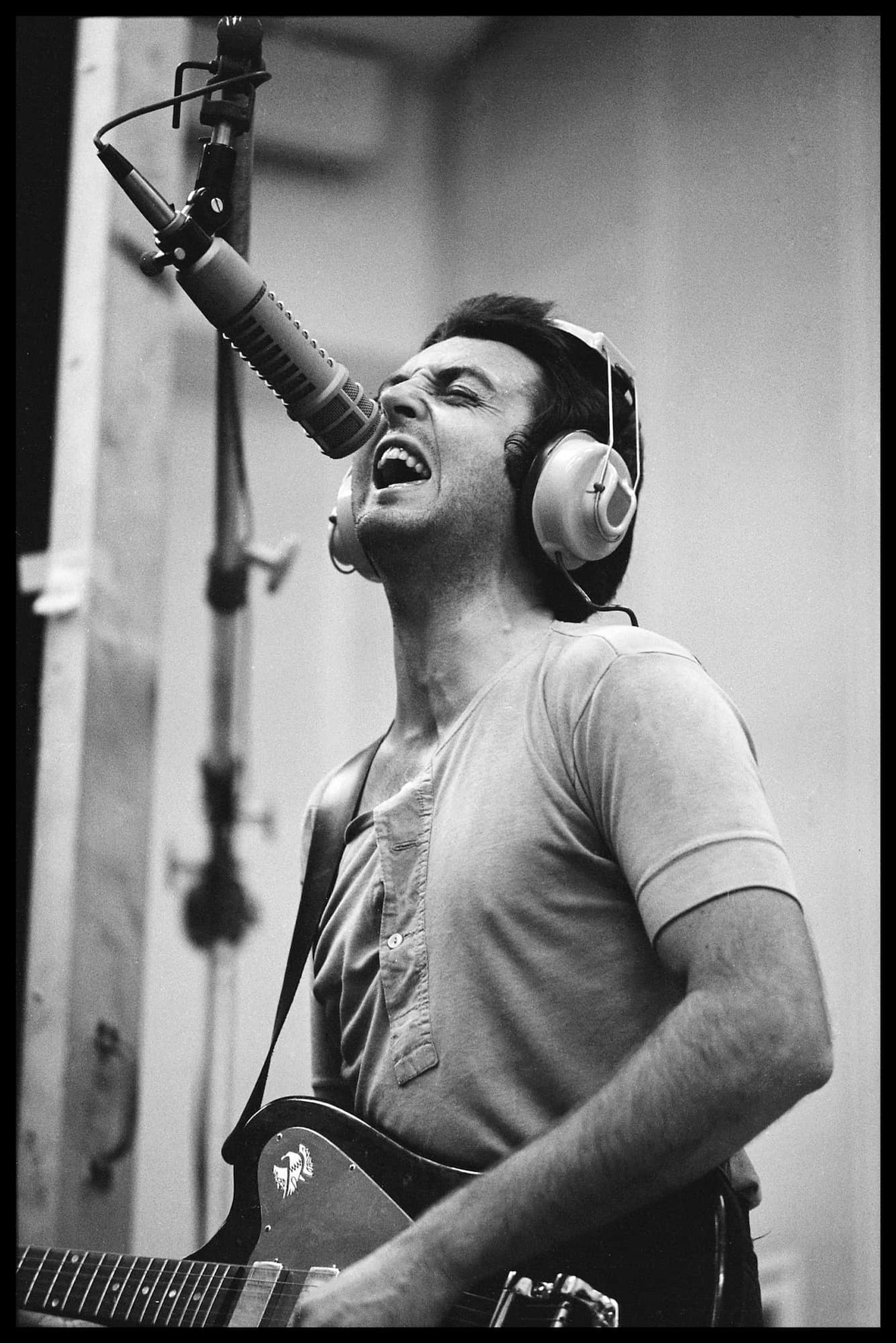 Black and white photo of Paul playing guitar and singing into a microphone 