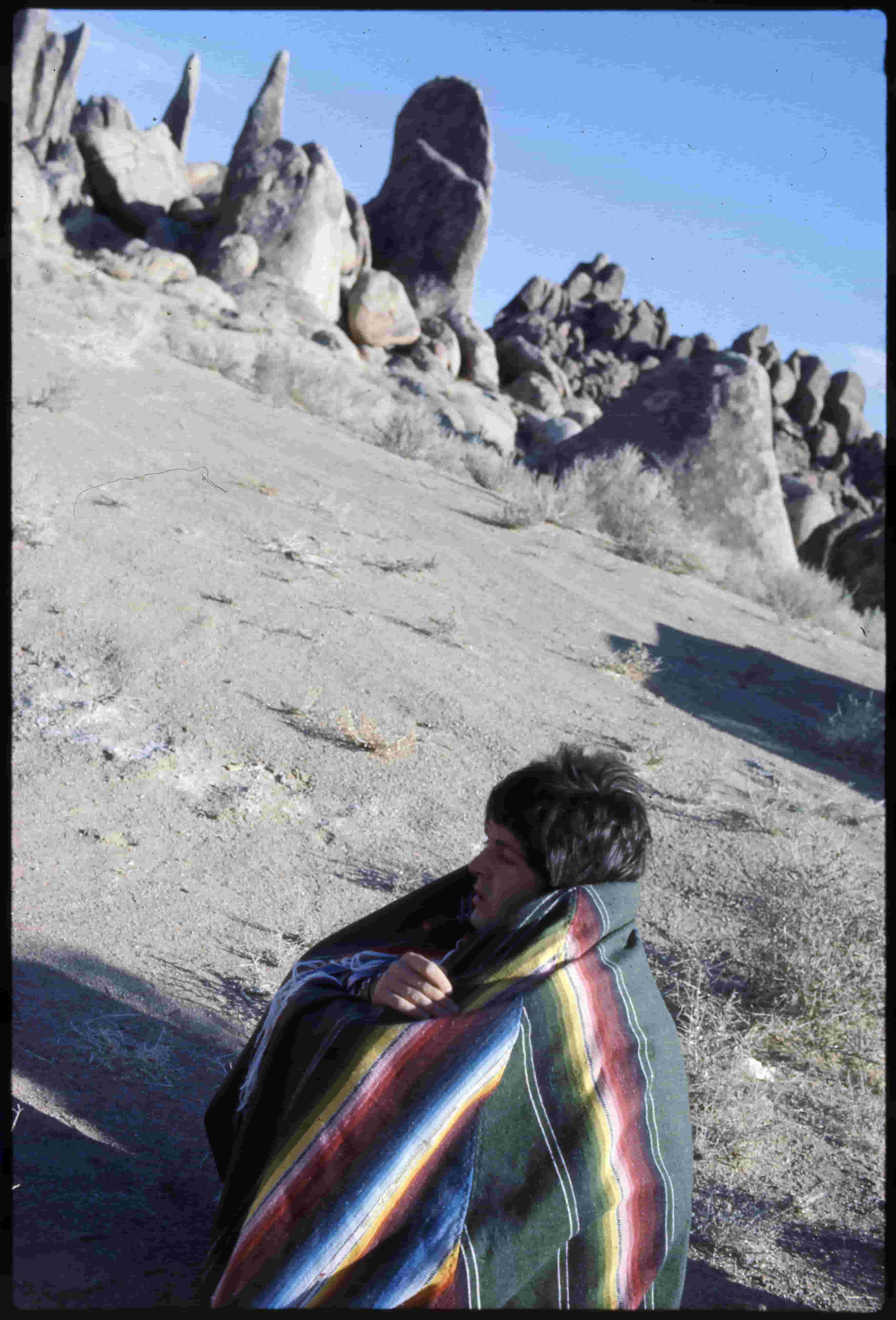 Paul crouching in the desert wearing a poncho