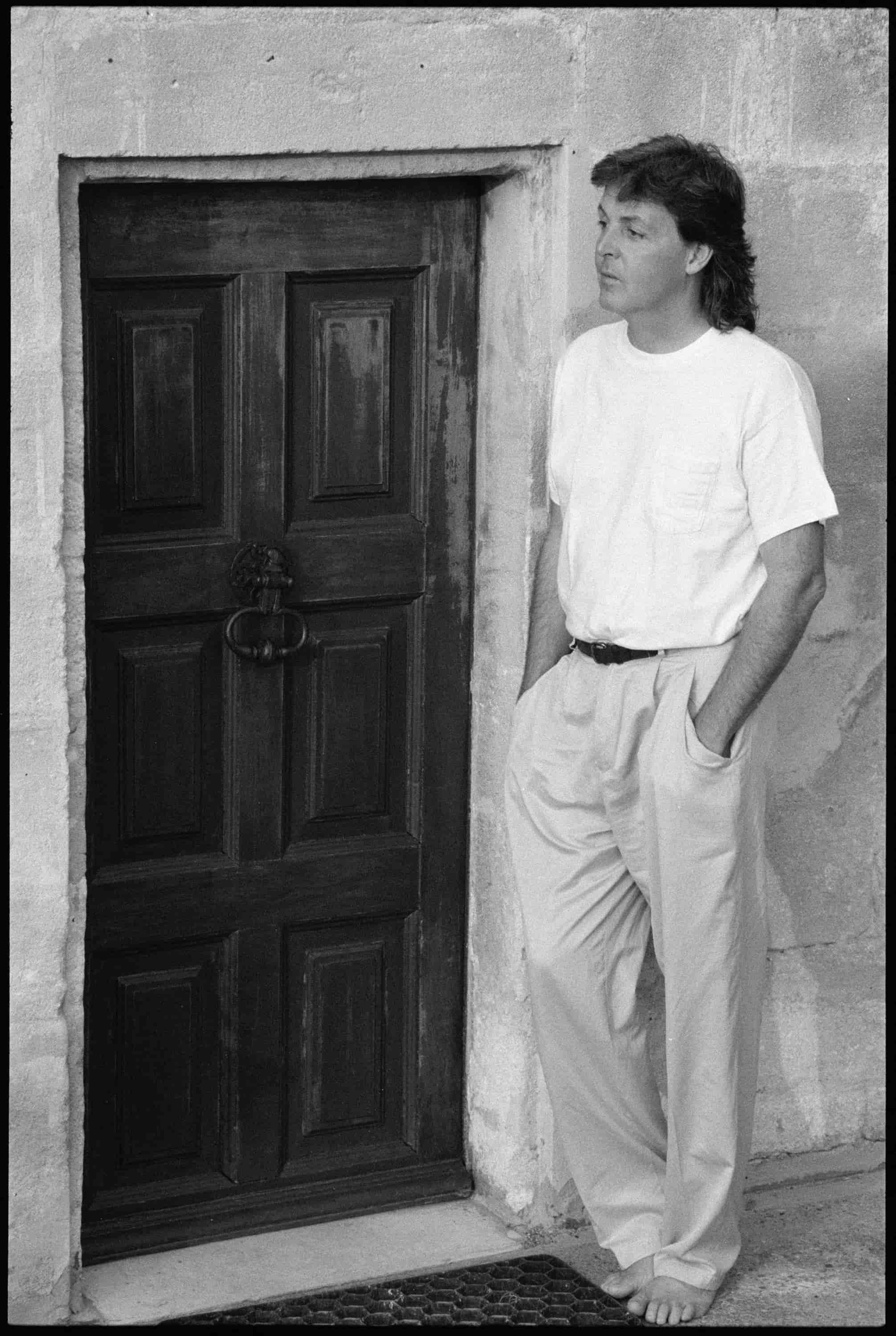 Black and white photo of Paul McCartney standing next to a door in south of France. 