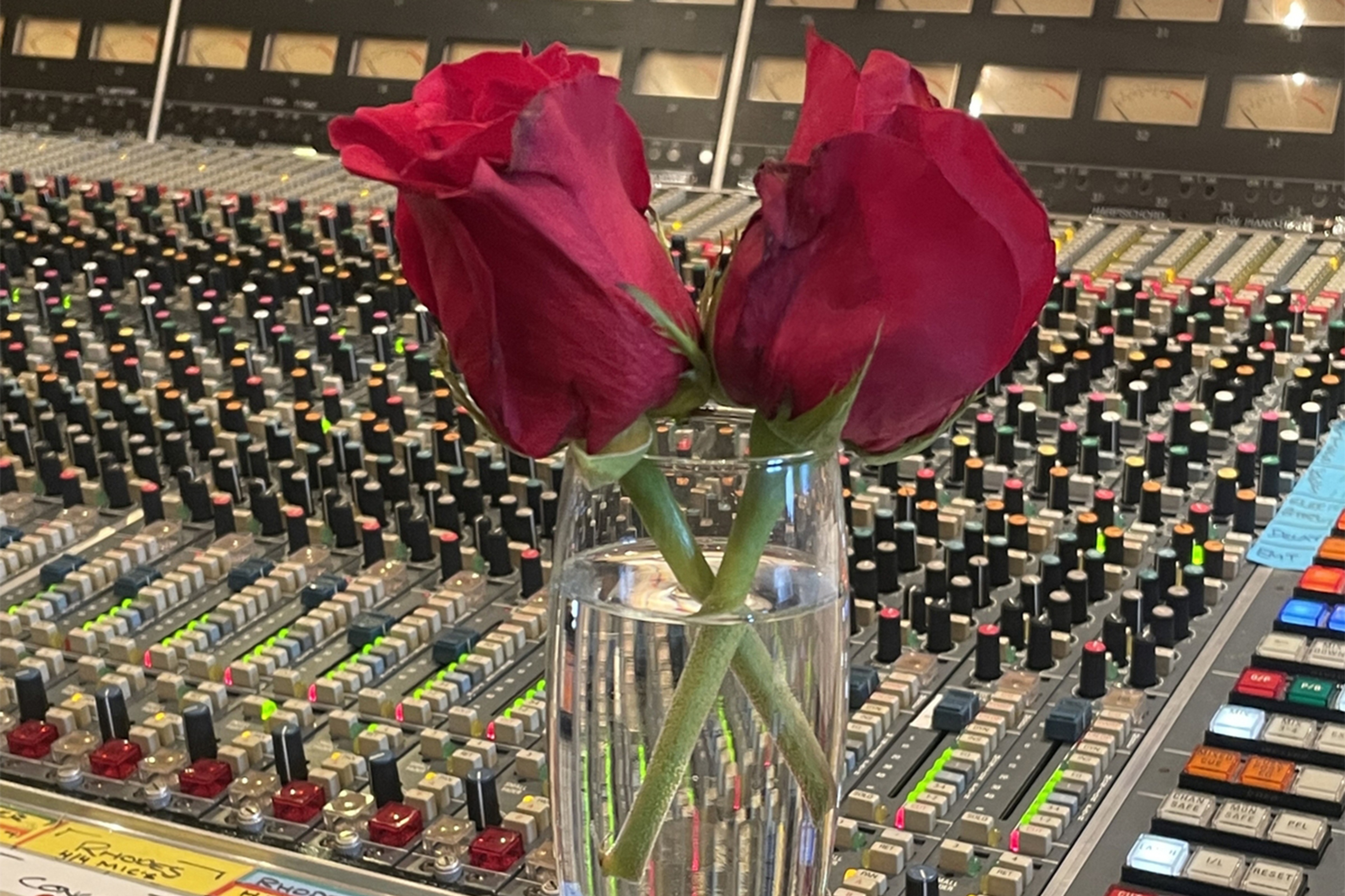 Two red roses in a glass, perched on a mixing desk