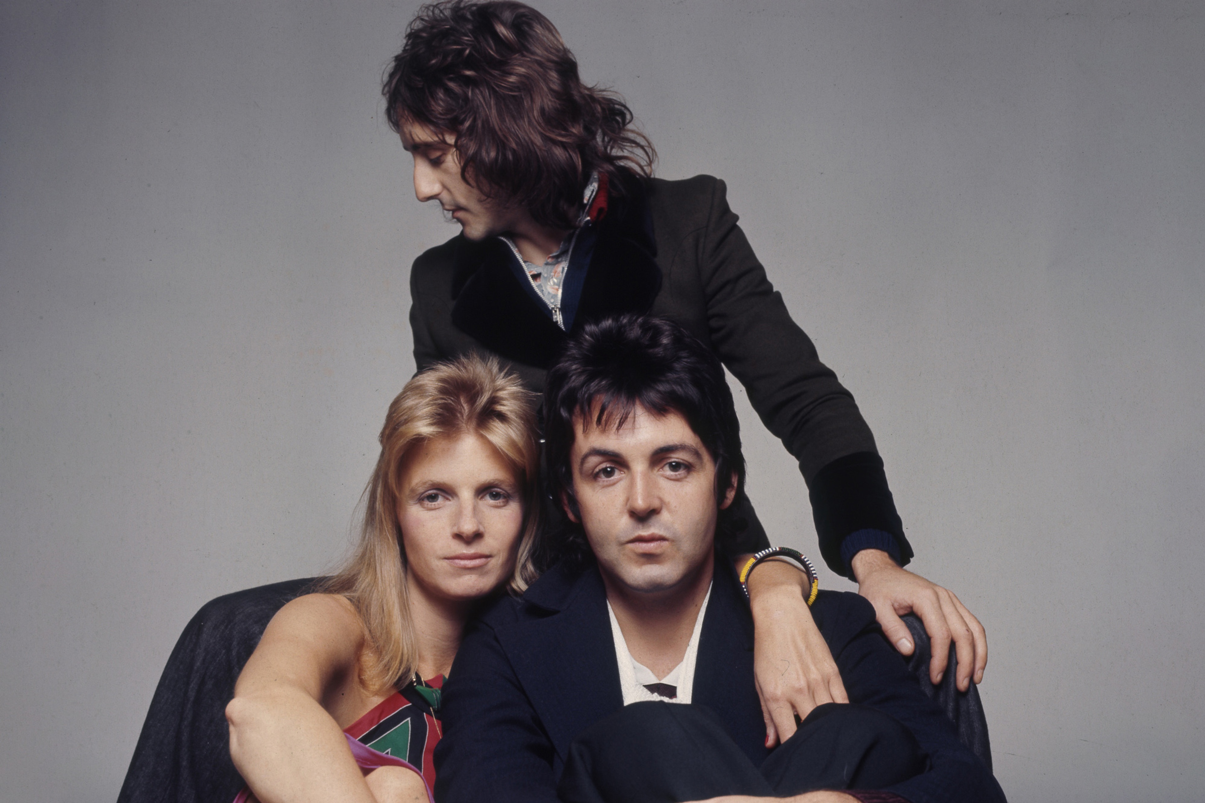 Denny Laine, Paul and Linda McCartney sitting in front of a grey background