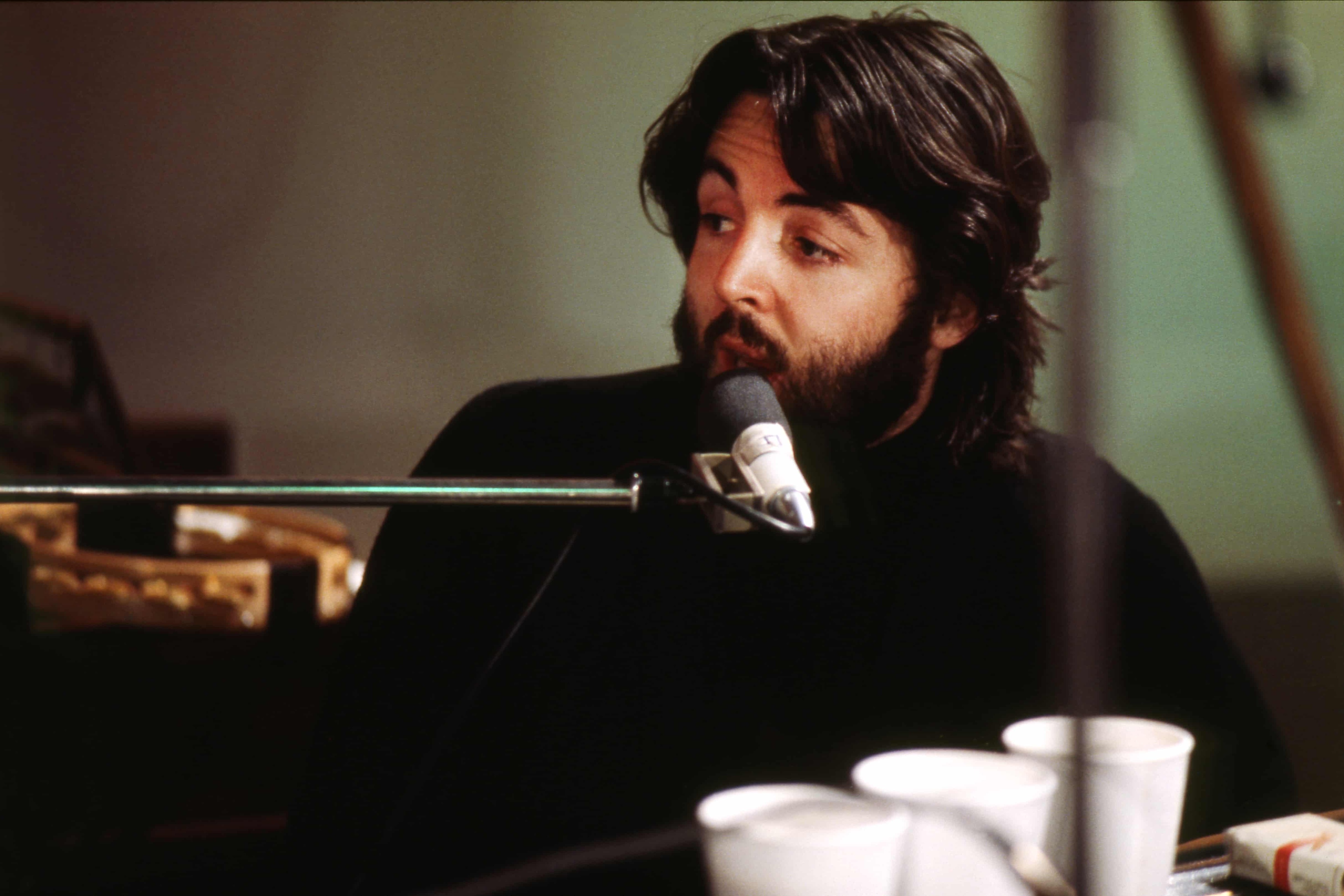 Paul sits at a piano singing into a mic