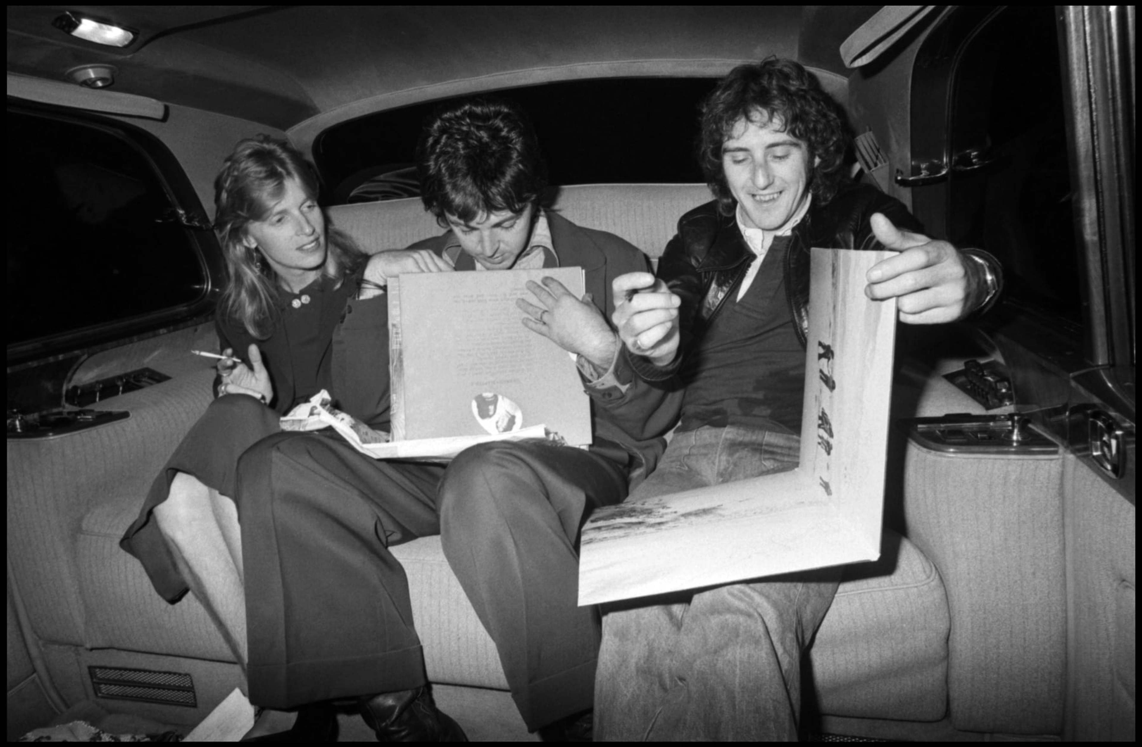 Linda, Paul, and Denny Laine holding books in the back of a car